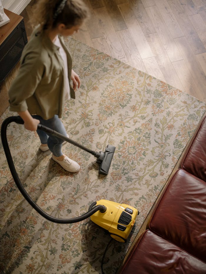 services-03 Overhead view of a woman vacuuming a carpet at home, highlighting cleanliness and housekeeping.