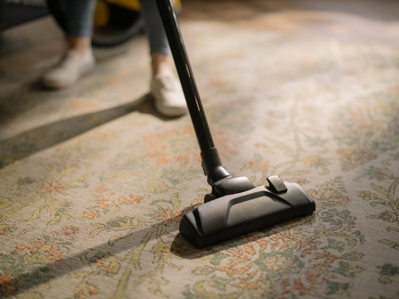 gallery-6 Close-up of a vacuum cleaner on a patterned carpet in a sunlit room, capturing a moment of household cleaning.